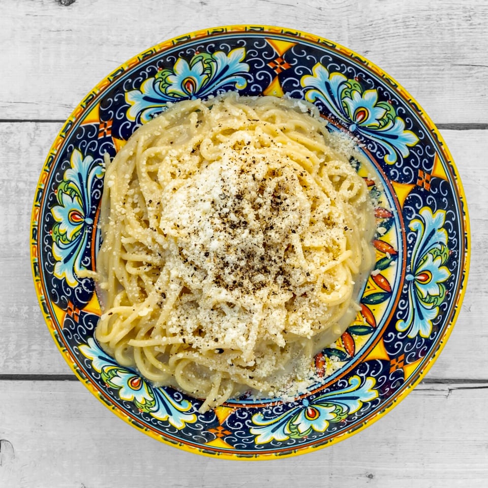 Cacio e pepe pasta with grated cheese and black pepper on a vibrant, patterned plate.