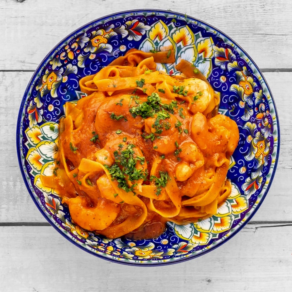 Fettuccine pasta with shrimp in a rich tomato sauce, garnished with fresh parsley, in a colorful bowl.