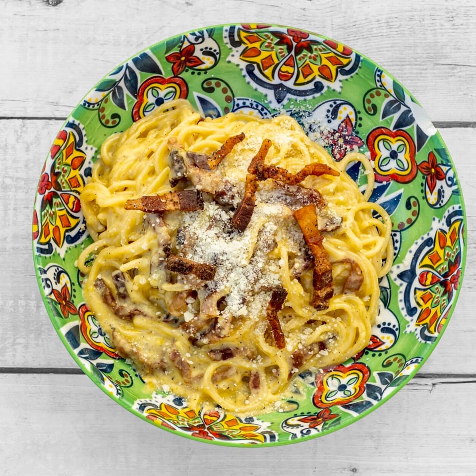 Spaghetti carbonara with crispy bacon and grated cheese in a vibrant green patterned bowl.