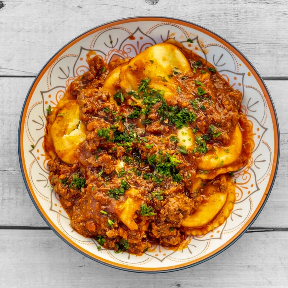 FABIOS PASTA's ravioli with rich meat sauce and fresh parsley in a decorative bowl.