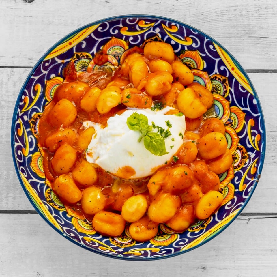 Gnocchi in red sauce with a dollop of burrata cheese and basil in a colorful bowl.